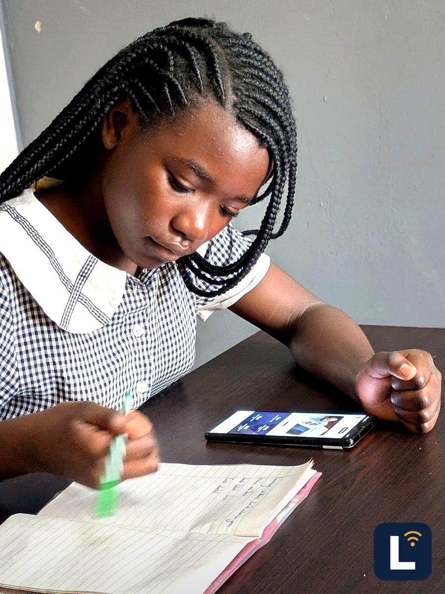 A learner writing notes at a desk with the lesson open on a phone